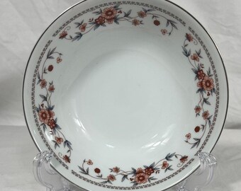 May include: White ceramic bowl with a floral design. The rim features a silver trim and a border of red and blue flowers. The bowl is supported by a clear plastic stand, showcasing its decorative pattern.