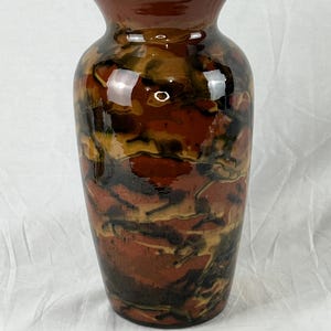 May include: A tall, ceramic vase with a glossy finish. The vase features a blend of colours, including shades of brown, black, and tan, creating a marbled effect. The vase has a wide body that tapers towards the top, with a narrow opening.