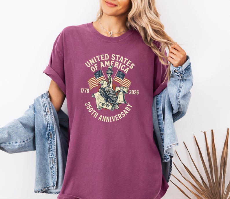 May include: A maroon t-shirt with a graphic commemorating the 250th anniversary of the United States of America. The design includes an eagle, flags, and the text "United States of America 250th Anniversary 1776-2026".