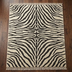 May include: A rectangular area rug featuring a high-contrast zebra stripe pattern in black and cream. The rug has a symmetrical design with a central spine and fringe detailing along the top and bottom edges, creating a textured appearance.