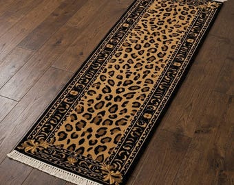 Puede incluir: Una alfombra de pasillo rectangular con un patrón central de leopardo en tonos bronceado y marrón, bordeada por un marco negro ancho con detalles florales dorados, terminada con flecos blancos en ambos extremos del tapiz.