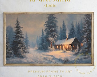 May include: A framed landscape painting depicts a snow-covered cabin nestled among tall evergreen trees. The cabin's windows glow warmly, and a path leads through the snowy forest. The text "la artesanía studio" and "PREMIUM FRAME TV ART" are visible.