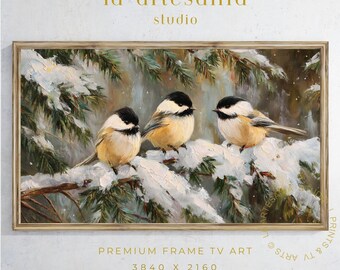May include: A framed painting featuring three chickadees perched on a snow-covered branch. The birds have black caps, white cheeks, and tan bodies. The artwork is set against a backdrop of snowy evergreen branches. The text "la artesanía studio" is at the top.