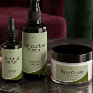 May include: A set of three skincare products including a black dropper bottle labeled Retinol Serum, a black pump bottle labeled Moisturizer Serum, and a white jar labeled Face Cream. Each container features a sage green label with black text.