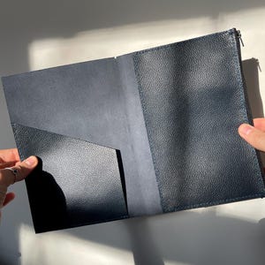 Peut inclure: Porte-documents en cuir bleu marine ouvert, avec une surface texturée. Le porte-documents a une poche sur le côté gauche et une fermeture éclair sur le côté droit. L'intérieur est bleu plus clair.