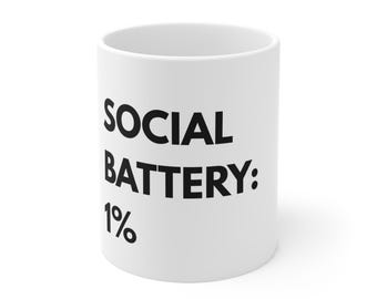 May include: White ceramic mug with the text "SOCIAL BATTERY: 1%" printed in black. The mug is cylindrical and appears to be empty. The mug is a standard size and shape for coffee or tea.