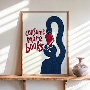 Puede incluir: Una lámina enmarcada con la silueta azul oscuro de una figura colocando un libro rojo en una abertura en la parte superior de su cabeza. El texto "consume more books" está escrito en rojo a la izquierda de la figura sobre un fondo crema.
