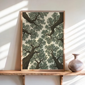 May include: A rectangular framed wall art print featuring a low-angle perspective of tree trunks and branches with dense green foliage against a pale cream sky. The artwork is displayed on a wooden shelf next to a round, textured ceramic vase.