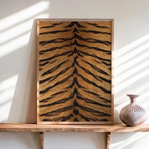 May include: A rectangular framed wall art piece featuring a detailed tiger fur pattern with orange, black, and brown stripes. The print is displayed in a light-toned wooden frame, positioned on a wooden shelf next to a small, round ceramic vase.