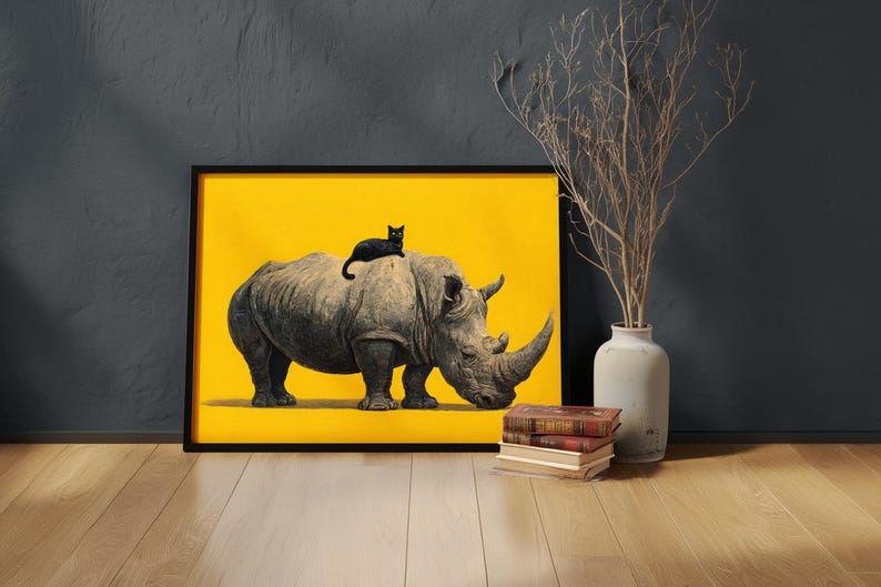 May include: A framed wall art print featuring a grey rhinoceros standing on a solid bright yellow background with a small black cat resting on its back. The artwork is displayed in a thin black frame, showcasing a high-contrast animal illustration.