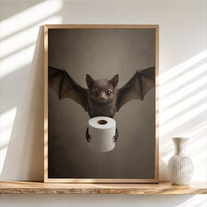 May include: A framed wall art print featuring a dark brown bat with large eyes and spread wings, holding a white roll of toilet paper in its claws. The background is a solid, muted dark gray, and the frame is a light-toned natural wood finish.