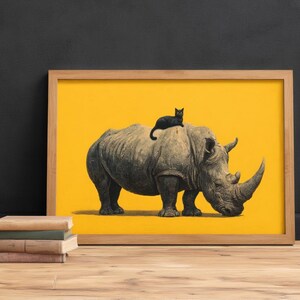 May include: A framed rectangular print featuring a detailed illustration of a large gray rhinoceros standing on a solid bright yellow background. A small black cat is perched on the back of the rhinoceros. The frame is made of light-colored wood.