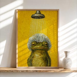 May include: A framed wall art print featuring a green frog wearing a clear plastic shower cap while standing under a shower head. The background is a solid, textured mustard yellow color, and the frog appears to be taking a shower.
