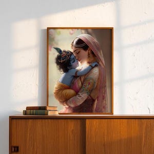 A framed painting of a woman embracing a child, likely a depiction of the Hindu deity Radha, is displayed on a wooden cabinet against a white wall.