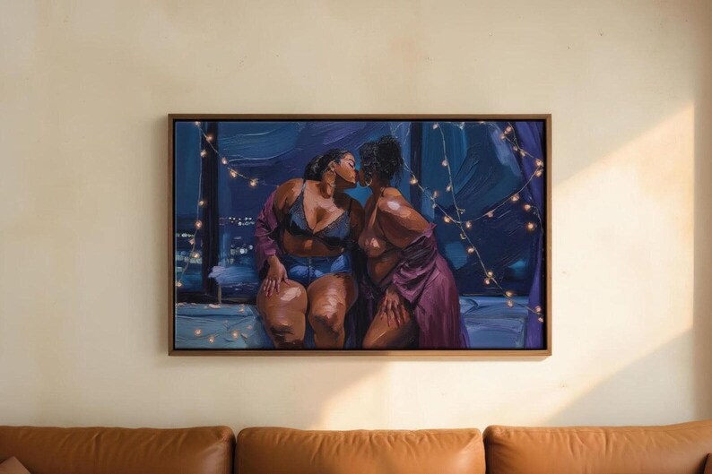 The image is a framed painting depicting two women in intimate poses, with one woman kissing the other. The painting is hung on a wall above a brown leather couch.