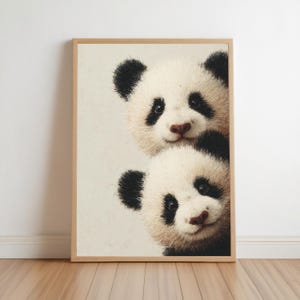 Könnte beinhalten: Ein gerahmter Kunstdruck mit einer texturierten Illustration von zwei vertikal übereinander angeordneten Pandagesichtern. Die Pandas haben weißes Fell mit schwarzen Flecken um Augen und Ohren vor einem hellen cremefarbenen Hintergrund.