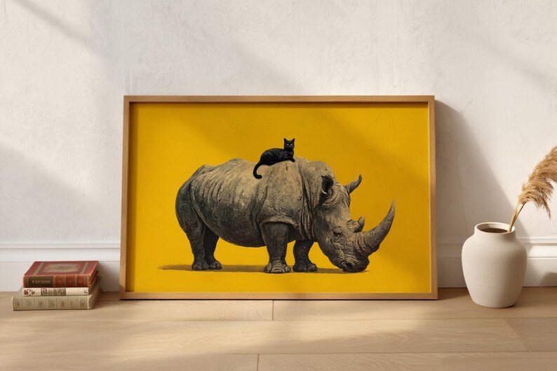 May include: A framed horizontal wall art print featuring a detailed illustration of a grey rhinoceros standing in profile with a small black cat resting on its back, set against a solid, vibrant mustard yellow background within a light wood frame.