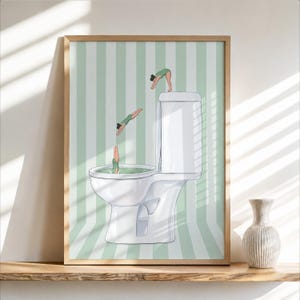 May include: A framed wall art print featuring a white toilet against a light green and white vertical striped background. Three figures in green swimsuits are depicted in various stages of diving into the toilet bowl water.