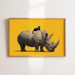 May include: A framed wall art print featuring a detailed illustration of a grey rhinoceros standing on a solid, vibrant yellow background. A small black cat is perched on the back of the rhinoceros. The artwork is enclosed in a light wood frame.