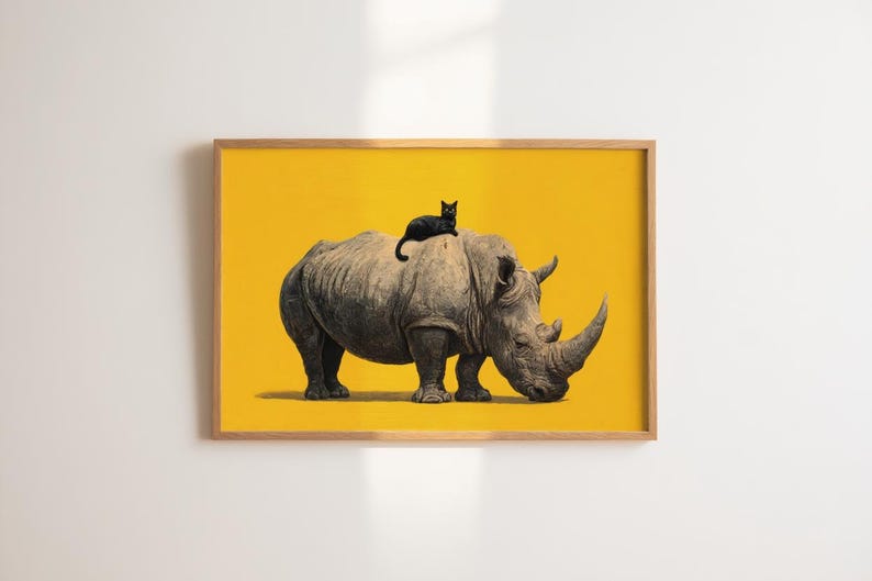 May include: A framed wall art print featuring a detailed illustration of a grey rhinoceros standing on a solid, vibrant yellow background. A small black cat is perched on the back of the rhinoceros. The artwork is enclosed in a light wood frame.
