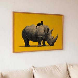 May include: A rectangular framed wall art piece featuring a black and white illustration of a rhinoceros with a small black cat sitting on its back, set against a solid, vibrant yellow background, enclosed in a light-toned wooden frame.