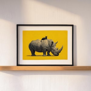 May include: A framed art print featuring a black and white illustration of a rhinoceros with a small black cat sitting on its back, set against a solid yellow background. The artwork is enclosed in a thin black frame with a white mat border.
