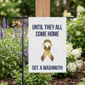 May include: A white garden flag featuring the navy blue text "UNTIL THEY ALL COME HOME". A gold ribbon graphic is below the text. The name "SGT. K WASHMUTH" is printed at the bottom in navy blue.