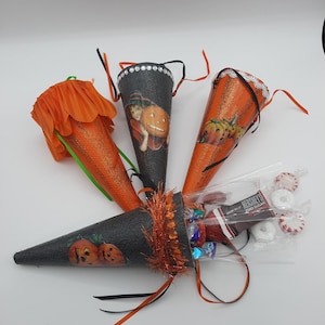 May include: Four Halloween treat cones in the image. Two are orange with glitter, one with a pumpkin graphic, and one with a witch graphic. The other two are black with pumpkin graphics. Each cone is decorated with ribbons and filled with sweets.
