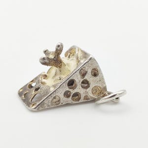 Peut inclure: Un charm argenté en forme de part de fromage percé de trous. Une petite figurine de souris détaillée est posée sur le fromage, qui présente un intérieur crémeux blanc cassé. Le charm est équipé d'une boucle d'attache.