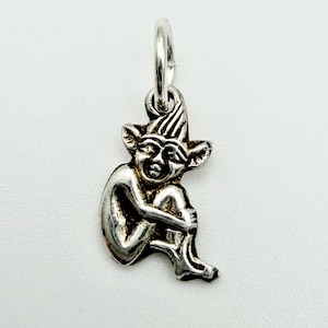 May include: A silver charm in the shape of a seated goblin or elf. The charm has a loop at the top for attaching to a necklace or bracelet. The goblin is detailed with pointed ears, a hat, and arms wrapped around its knees.