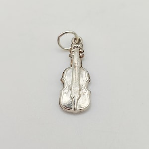 May include: A silver violin charm with intricate detailing. The charm features a loop for attaching to jewellery. The violin's body and strings are clearly defined. The charm is likely made of a metal alloy.