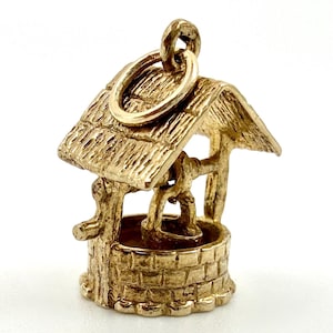 May include: A gold-colored charm in the shape of a wishing well. The well features a brick base, a sloped roof, and a small bucket. The charm has a loop at the top for attaching to a bracelet or necklace.