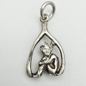 May include: A silver-toned pendant featuring a seated goblin figure within a wishbone-shaped frame. The goblin has pointed ears and a smiling expression. The pendant includes a loop for attaching to a chain or bracelet.