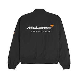 May include: Black bomber jacket featuring the McLaren Formula 1 Team logo in white and orange. The jacket has a stand-up collar, long sleeves, and a ribbed hem. The McLaren logo is prominently displayed on the back.