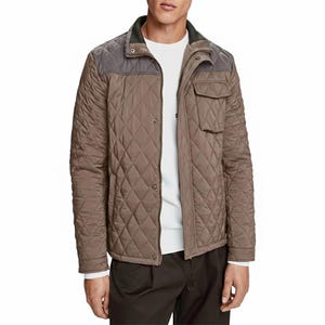 Puede incluir: Chaqueta acolchada marrón con canesú gris y cuello verde oscuro. La chaqueta tiene cierre de botones, un bolsillo en el pecho y un patrón de diamantes. El modelo lleva una camisa blanca debajo.