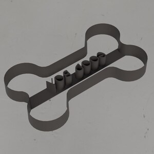 May include: A dark gray metal dog bone-shaped cookie cutter. The word "PAWSOME" is cut out in the center of the bone. The cutter is designed for making dog treats or cookies.