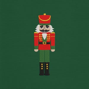 May include: Embroidered image of a toy soldier nutcracker. The nutcracker is dressed in a red jacket, green pants, and black boots. It has a white wig and mustache, and a red hat with gold trim. The background is a solid dark green.