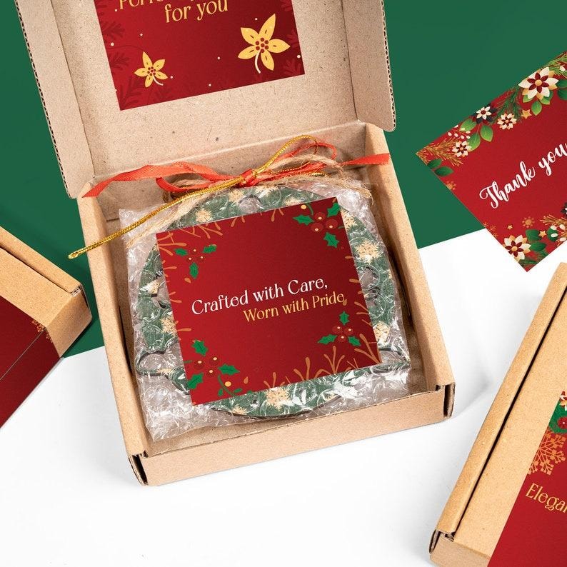 May include: A Christmas ornament in a cardboard box, wrapped in bubble wrap and tied with a red ribbon. The ornament is green and white with a floral design. A red card with the text "Crafted with Care, Worn with Pride" is on top.
