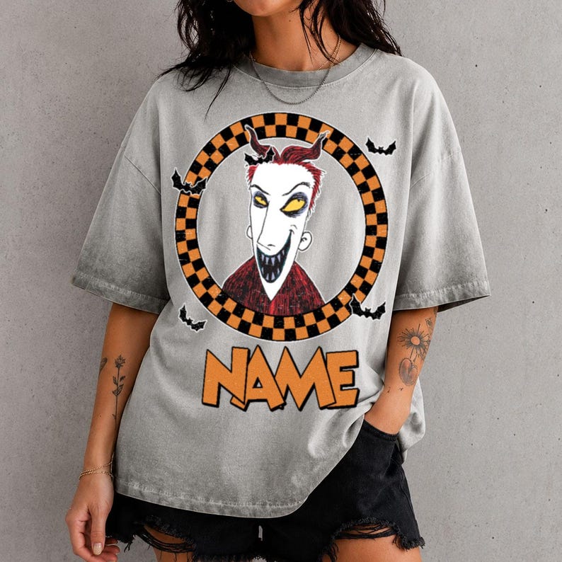 May include: A gray acid-wash t-shirt featuring a graphic of a character with spiky red hair and a wide grin inside a black and orange checkered circle. Small black bats surround the circle, and the word NAME is printed in orange below it.
