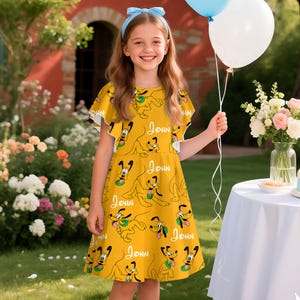 May include: A yellow dress featuring a repeating pattern of a cartoon dog and the name "John" in white script. The dress has short sleeves and a flared skirt. The girl is holding balloons.