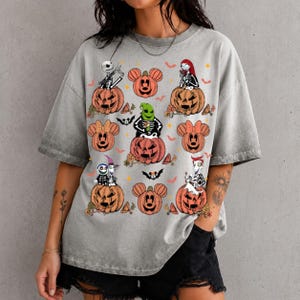 May include: A grey acid-wash t-shirt featuring a graphic print of various characters from The Nightmare Before Christmas sitting in or on orange pumpkins, interspersed with orange Mickey Mouse-shaped pumpkins, small bats, and orange stars.