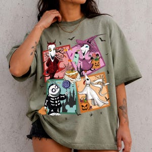 Może przedstawiać: Oliwkowozielony t-shirt z kr&oacute;tkim rękawem z nadrukiem graficznym składającym się z czterech kwadratowych paneli przedstawiających postacie z Miasteczka Halloween, w tym Jacka Skellingtona, Sally, Zero i Oogie Boogie, w otoczeniu małych czarnych nietoperzy.