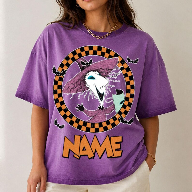 Puede incluir: Una camiseta morada de manga corta con un gr&aacute;fico de un personaje con sombrero y t&uacute;nica morados dentro de un c&iacute;rculo a cuadros negros y naranjas. El dise&ntilde;o incluye peque&ntilde;os murci&eacute;lagos negros y la palabra NAME en letras naranjas grandes.