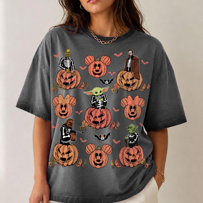 May include: A charcoal gray short-sleeve t-shirt featuring a Halloween-themed graphic print. The design includes various orange jack-o'-lanterns with mouse-ear shapes, small bats, and several characters wearing skeleton costumes sitting on pumpkins.