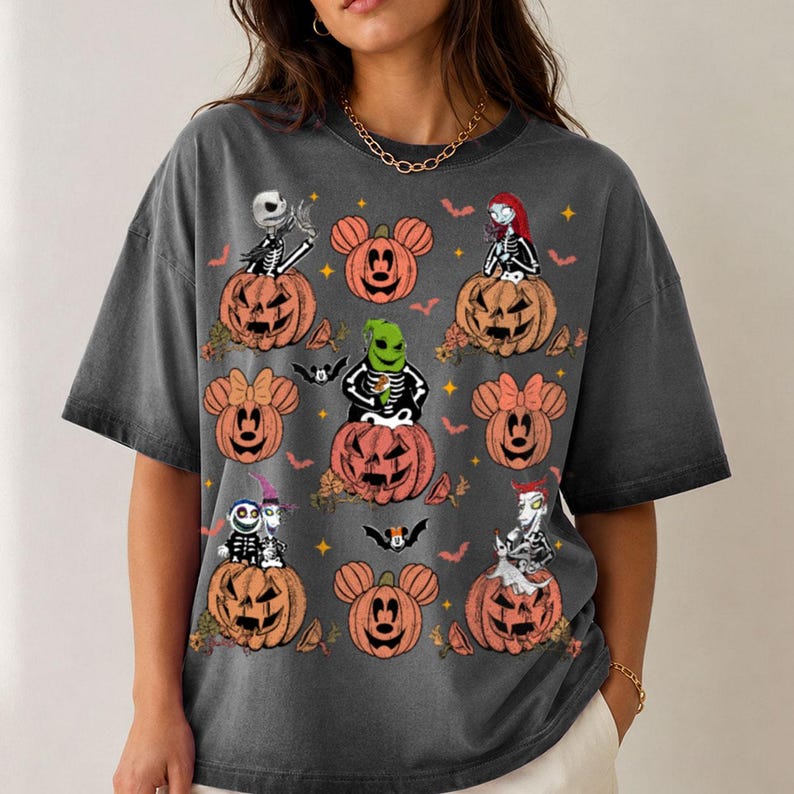 May include: A charcoal grey short-sleeve t-shirt featuring a graphic print of various characters from The Nightmare Before Christmas sitting in orange jack-o'-lanterns, interspersed with Mickey Mouse-shaped pumpkins, bats, and small yellow stars.