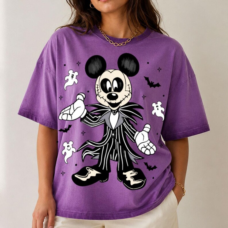 May include: A purple short-sleeve t-shirt featuring a graphic print of a character resembling Mickey Mouse dressed in a black and white pinstriped suit with a skull-like face, surrounded by small white ghost figures and black bat silhouettes.