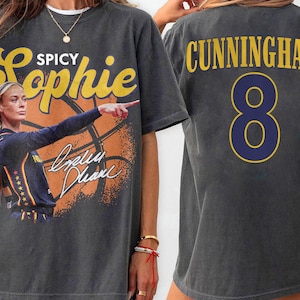 May include: A charcoal gray short-sleeve t-shirt featuring a vintage-style graphic of a basketball player with the text Spicy Sophie and a signature. The back of the shirt displays the name CUNNINGHAM in yellow letters above the large number 8.
