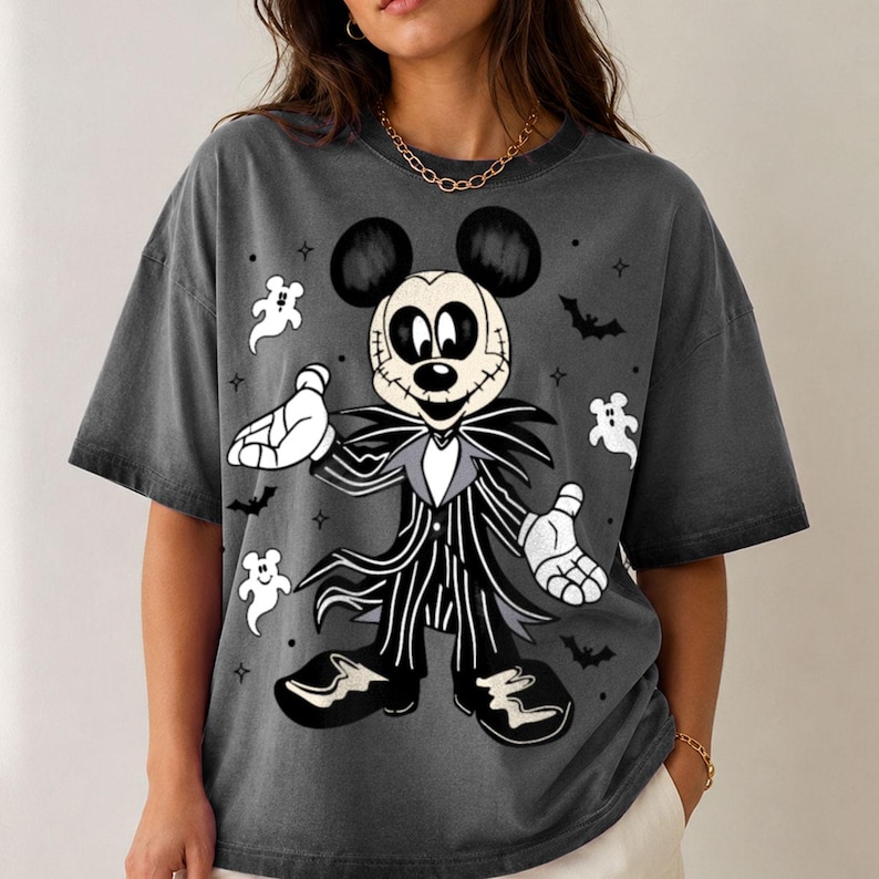 May include: A charcoal gray short-sleeve t-shirt featuring a graphic of a character resembling Mickey Mouse dressed in a black and white pinstriped suit. The design includes small white ghost figures, black bats, and star accents surrounding the character.