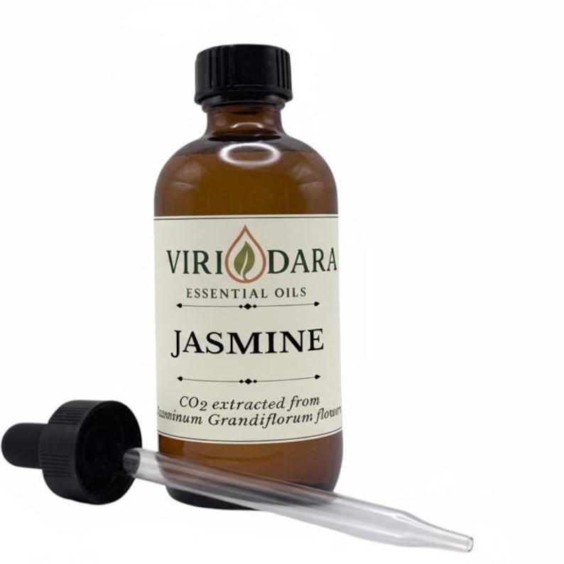 May include: A brown glass bottle of jasmine essential oil with a black cap and a glass dropper. The label reads "Viri Dara Essential Oils" and "Jasmine". The dropper is lying next to the bottle. The oil is extracted from Jasminum Grandiflorum flowers.