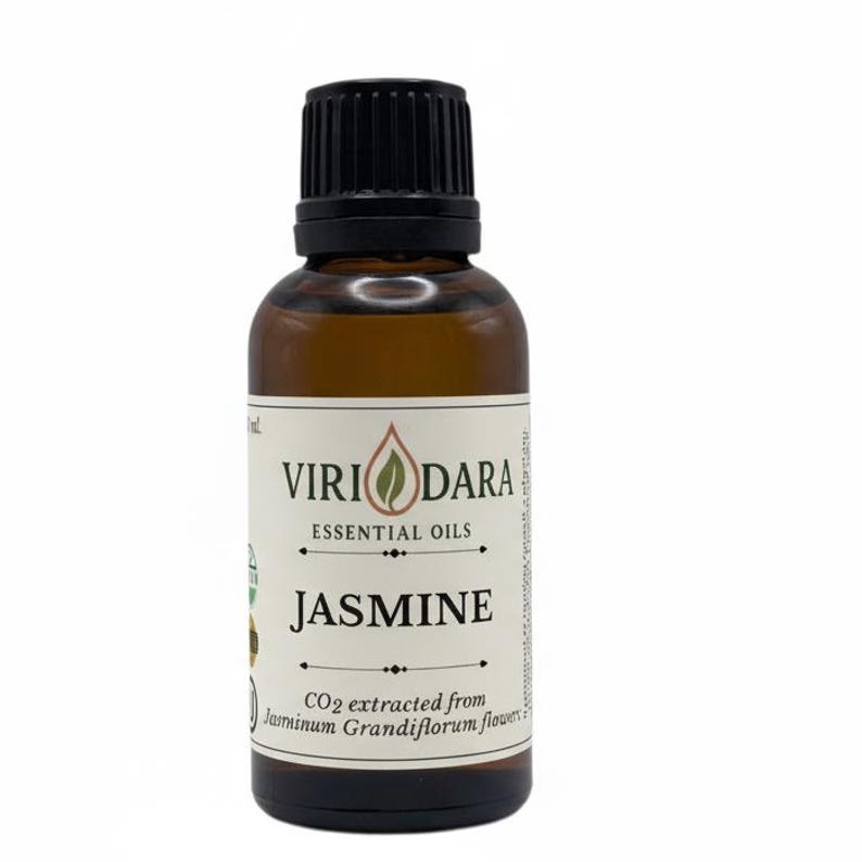 May include: A brown glass bottle of jasmine essential oil with a black cap. The label reads "Viri Dara Essential Oils" and "Jasmine". The bottom of the label states "CO2 extracted from Jasminum Grandiflorum flowers".